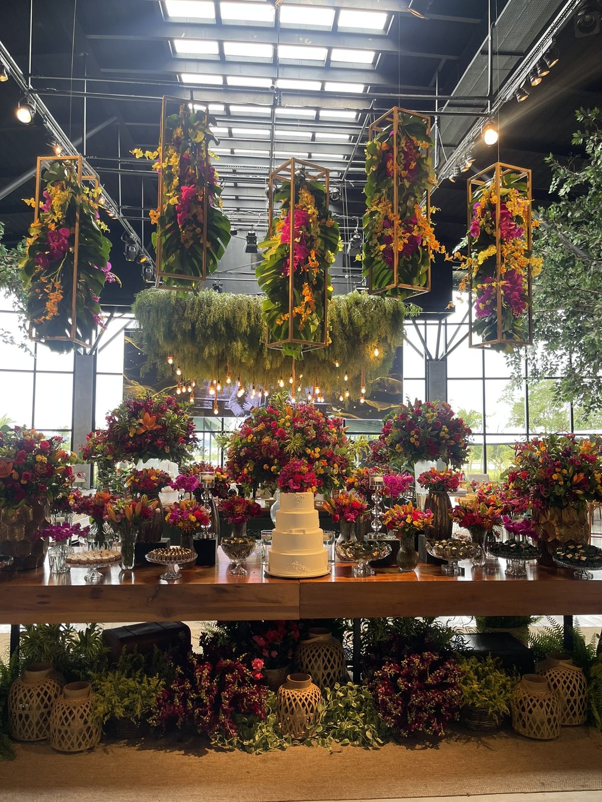 Mesa de bolo e doces com flores coloridas suspensas no casamento de Camila e Giovanni