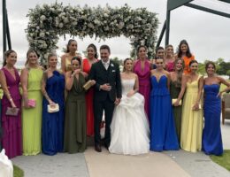 Camila e Giovanni com as madrinhas de vestidos coloridos diante do arco de flores