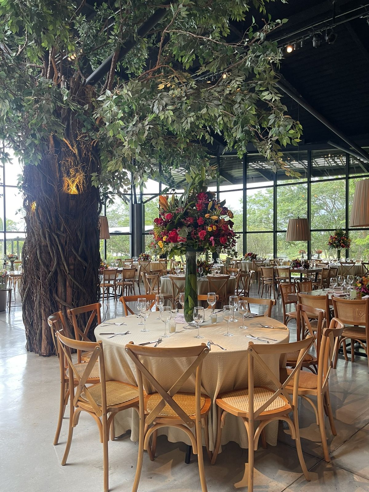 Salão da festa no Chez Bisutti Garden com árvore central e arranjos de flores
