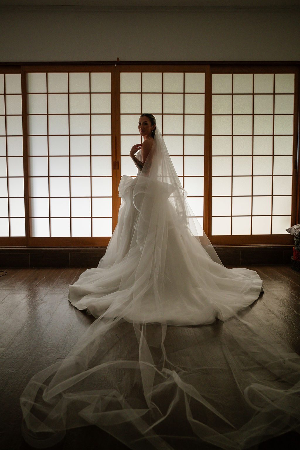 Camila de vestido e véu longo diante das portas de shoji